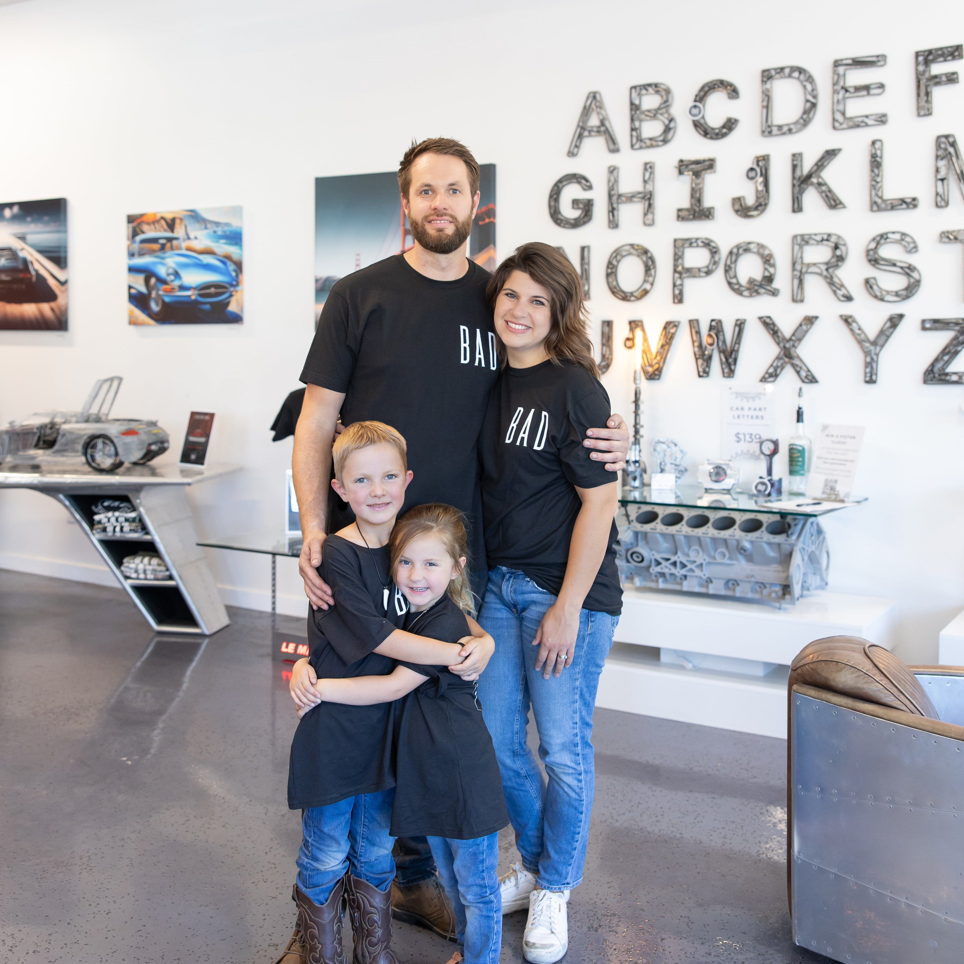Family of four posing together in a modern interior setting with a wall displaying letters.