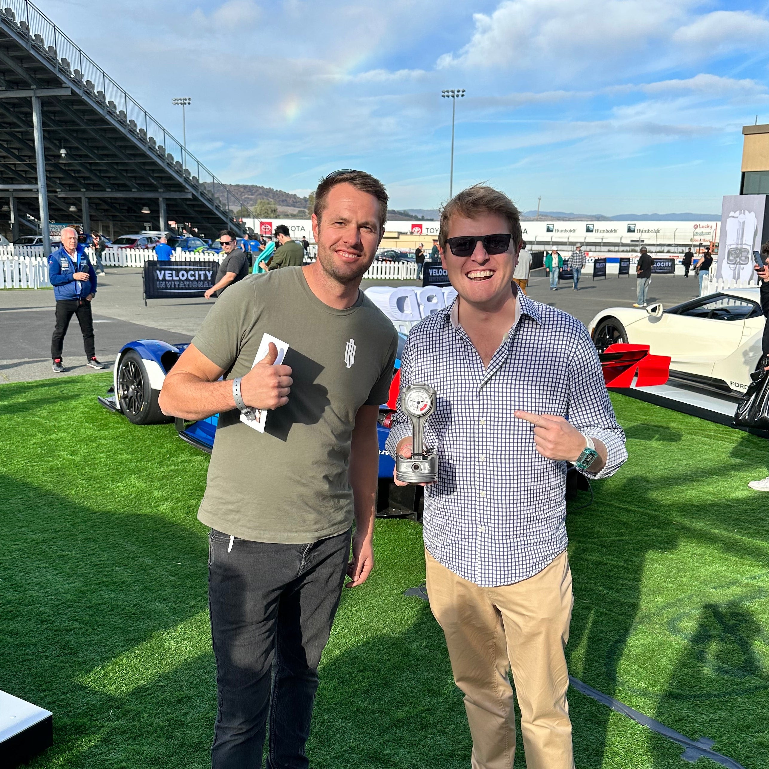 Two men standing on a grassy area with a clear blue sky and stadium in the background.