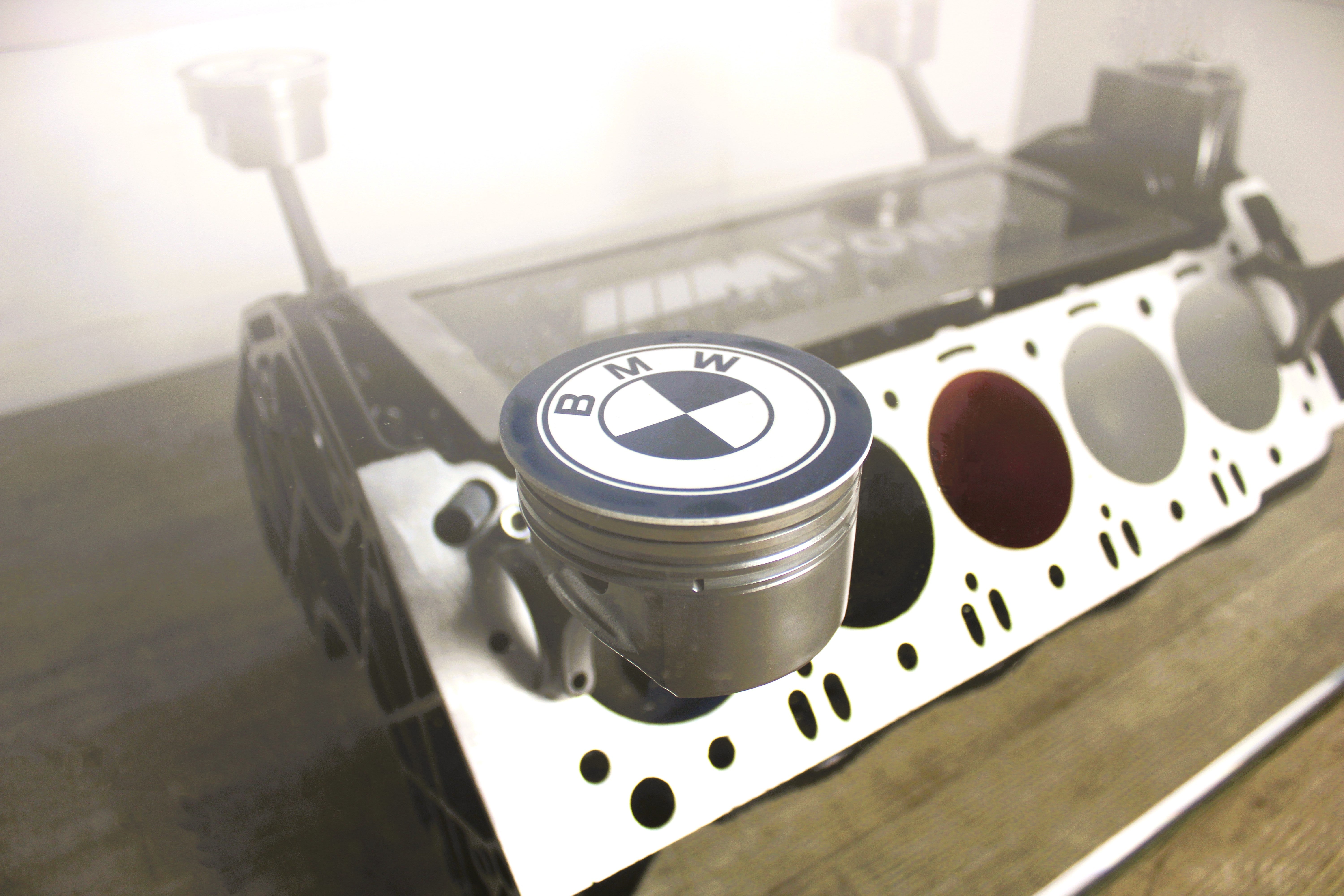 A close-up of the BMW logo on a BMW M Series V10 engine block coffee table painted in the BMW M-Power color scheme without its glass top, the M-Power logo displayed across the piece, and the BMW logo on each of the four car pistons.