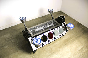 BMW M Series V10 engine block coffee table painted in the BMW M-Power color scheme without its glass top, the M-Power logo displayed across the piece, and the BMW logo on each of the four car pistons.