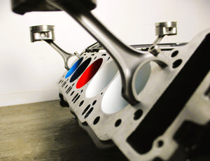 A close-up side view of a BMW M Series V10 engine block coffee table painted in the BMW M-Power color scheme without its glass top.