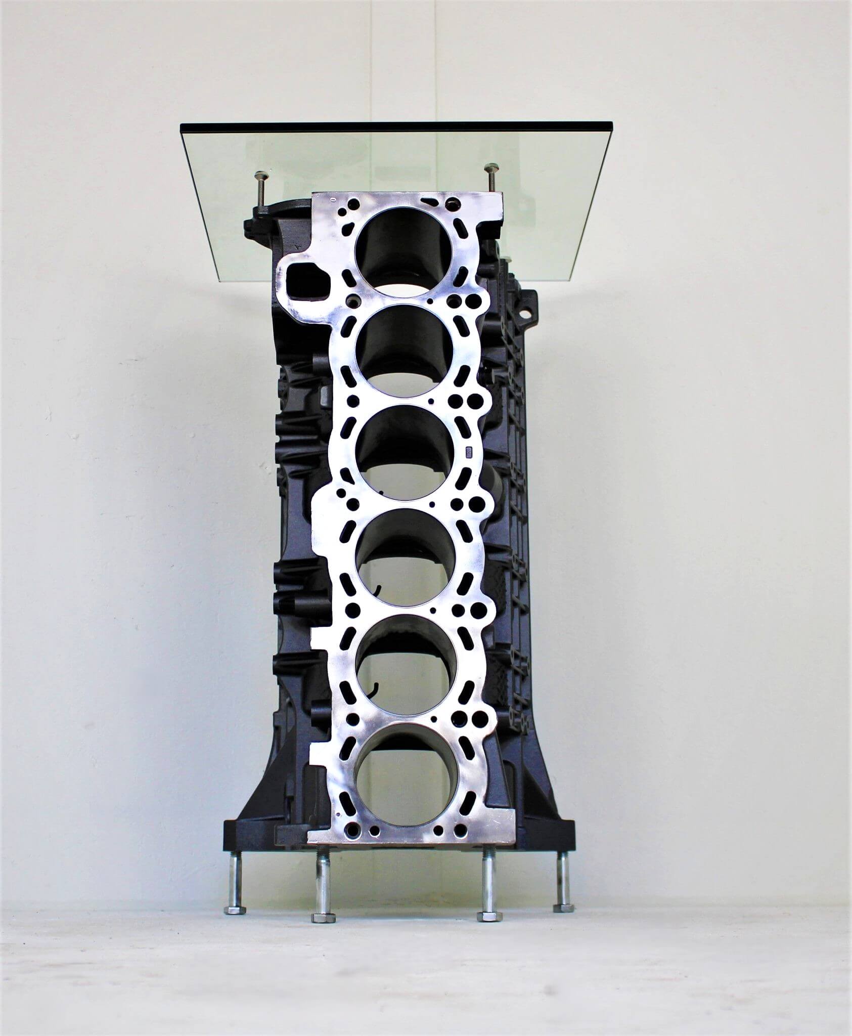 Wine rack table handcrafted from a genuine BMW car engine block finished in gray and silver with a square glass top.