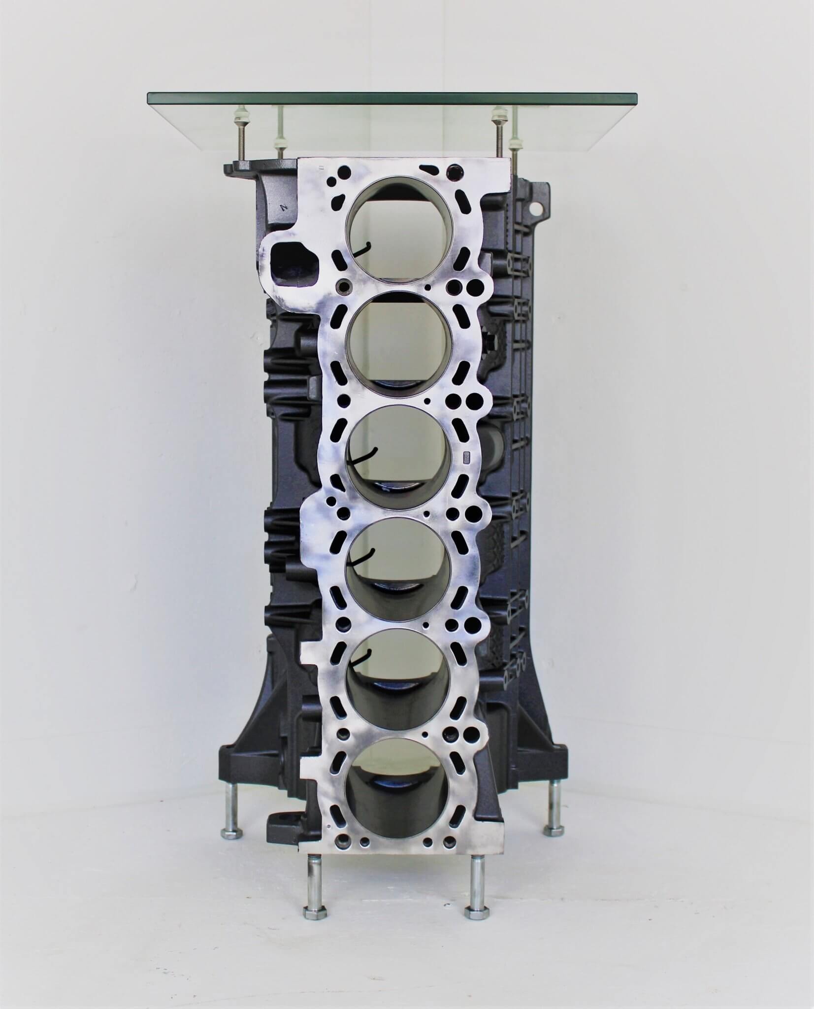 Wine rack table handcrafted from a genuine BMW car engine block finished in gray and silver with a square glass top.