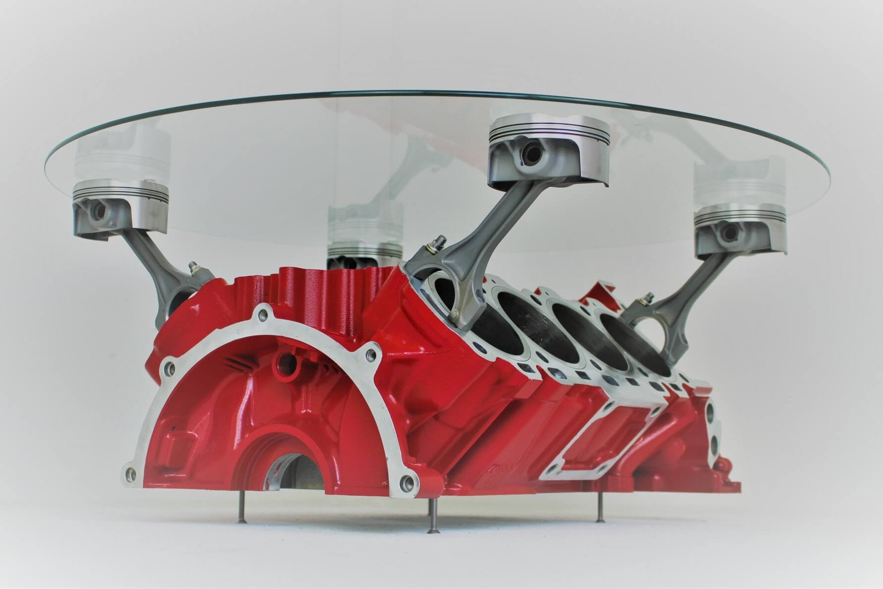 Coffee tables handcrafted from genuine car engines with various colored finishes, logos displayed, and glass top shapes.