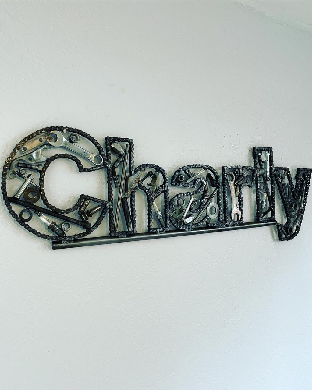 Hand-welded letter monogram decorations outlined with timing chain and filled in entirely with genuine polished car engine components with a glossy finish.