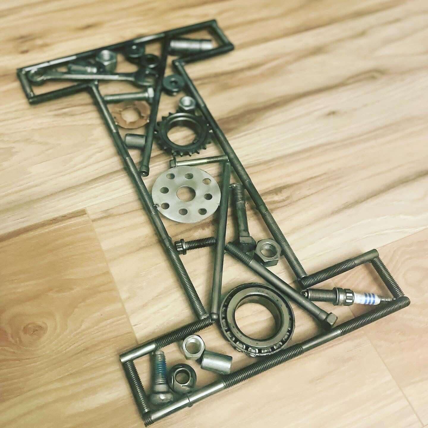 Hand-welded letter monogram decorations outlined with timing chain and filled in entirely with genuine polished car engine components with a glossy finish.