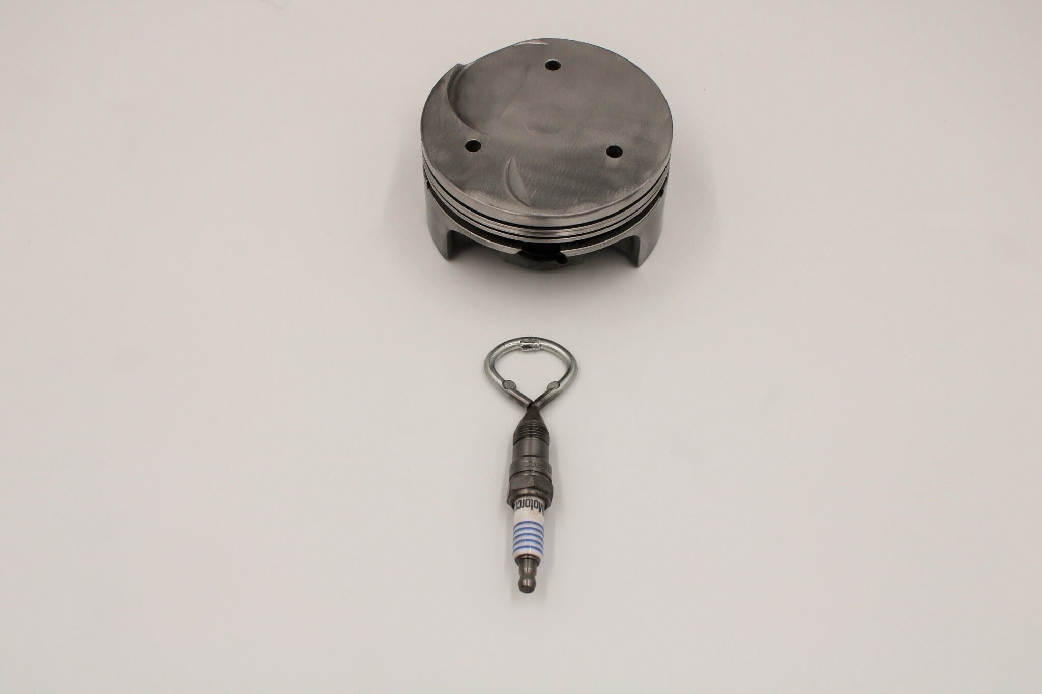 Barware set handcrafted from genuine car engine components - a polished car engine piston holder with a bottle opener, corkscrew, and stopper made from spark plugs.