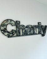 Load image into Gallery viewer, A name sign spelling &quot;Charly&quot; hanging on a wall, each letter made out of car parts and outlined with timing chain.
