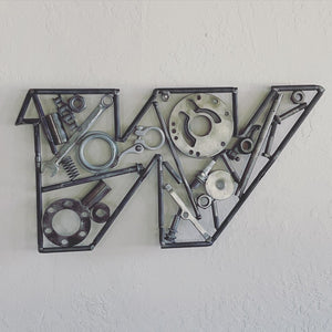 A letter W made out of real car parts hanging on a wall, outlined with screws.