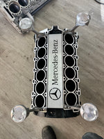 Load image into Gallery viewer, Birds-eye view of a Mercedes V12 engine block coffee table finished in black and silver without its glass top, the Mercedes Benz logo displayed in the center.
