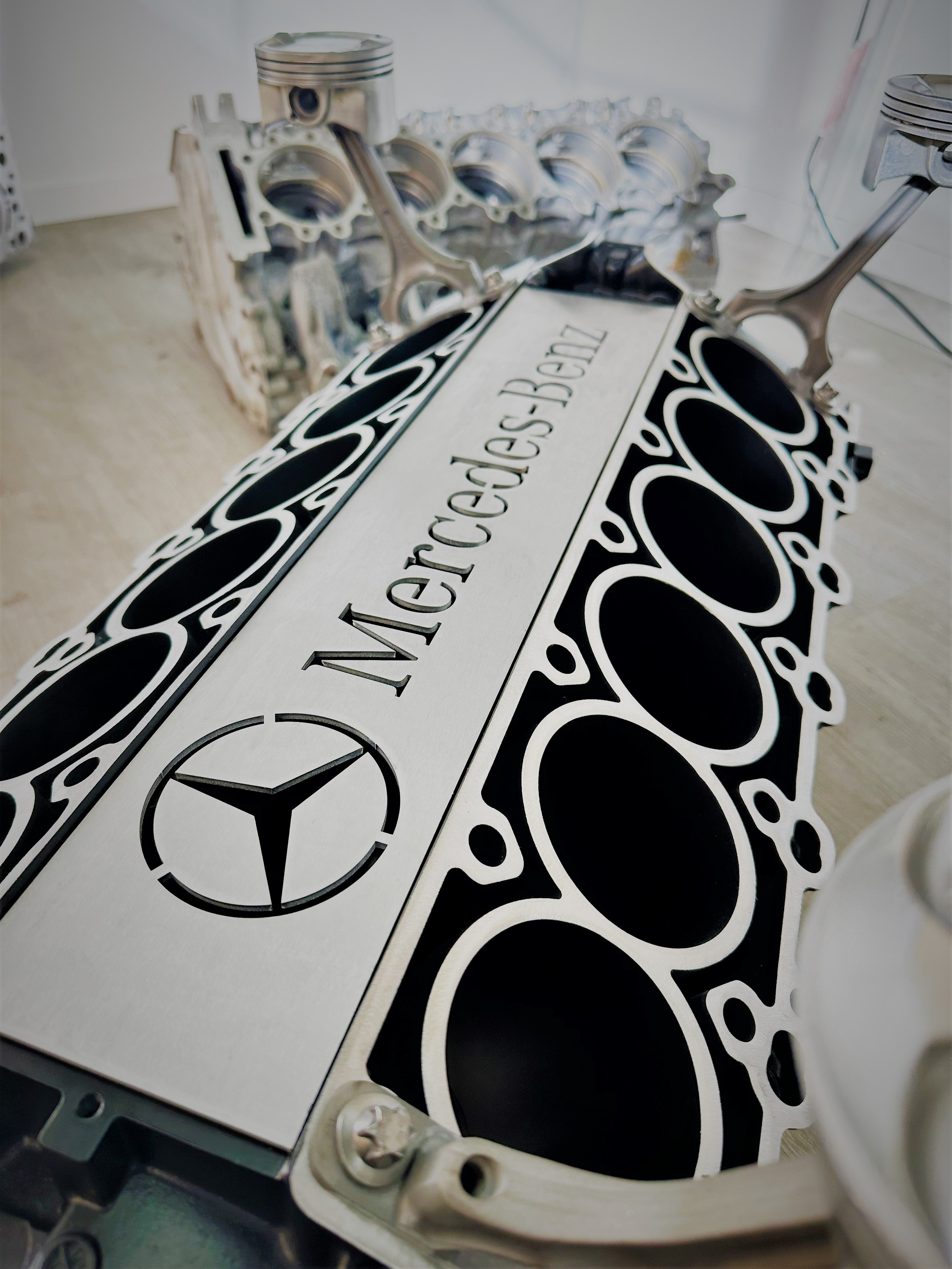 Close-up view of the Mercedes Benz logo displayed in the center of a Mercedes V12 engine block coffee table, finished in black and silver.