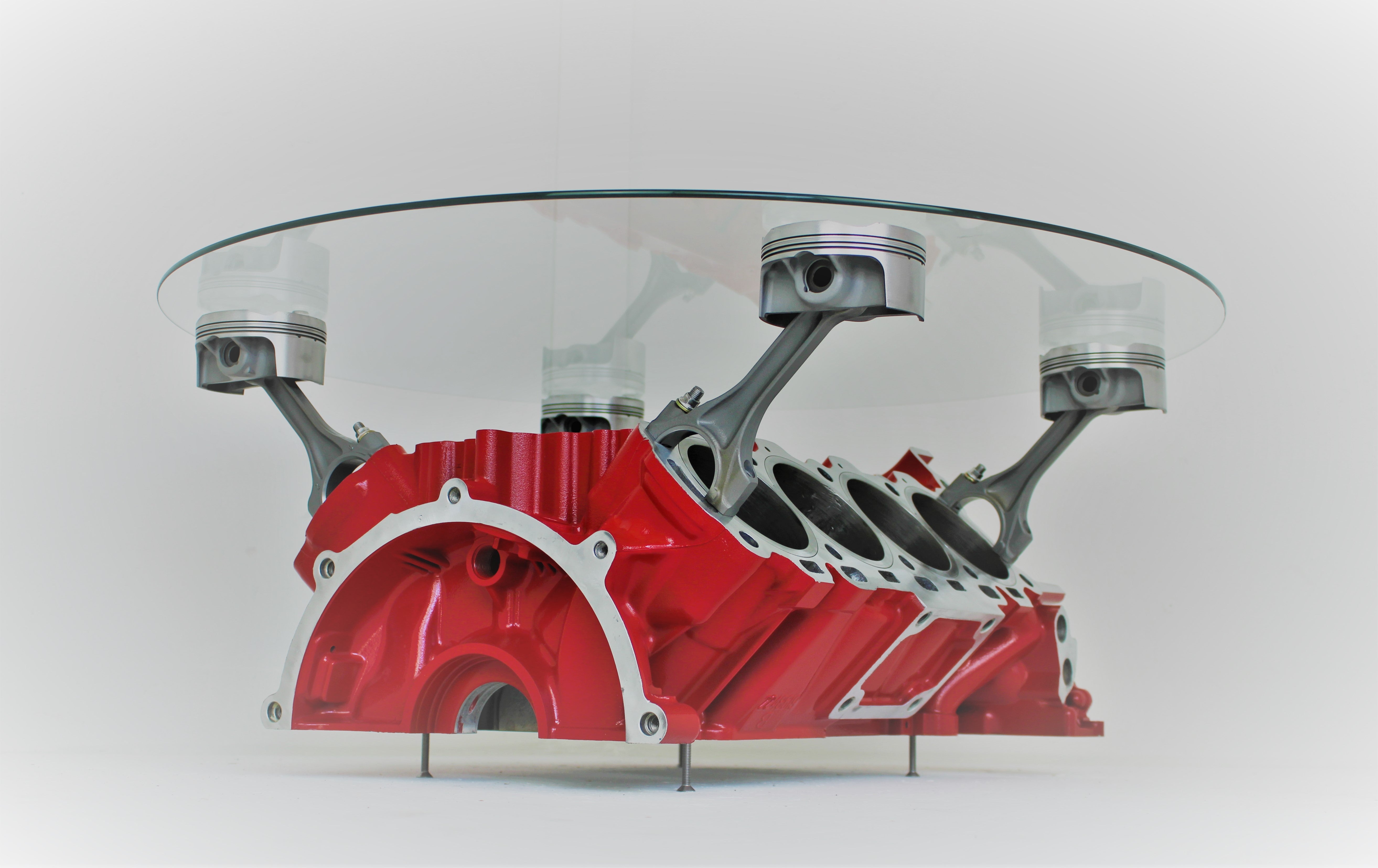 Engine block coffee table painted red, with its round glass top being held up by car engine pistons.