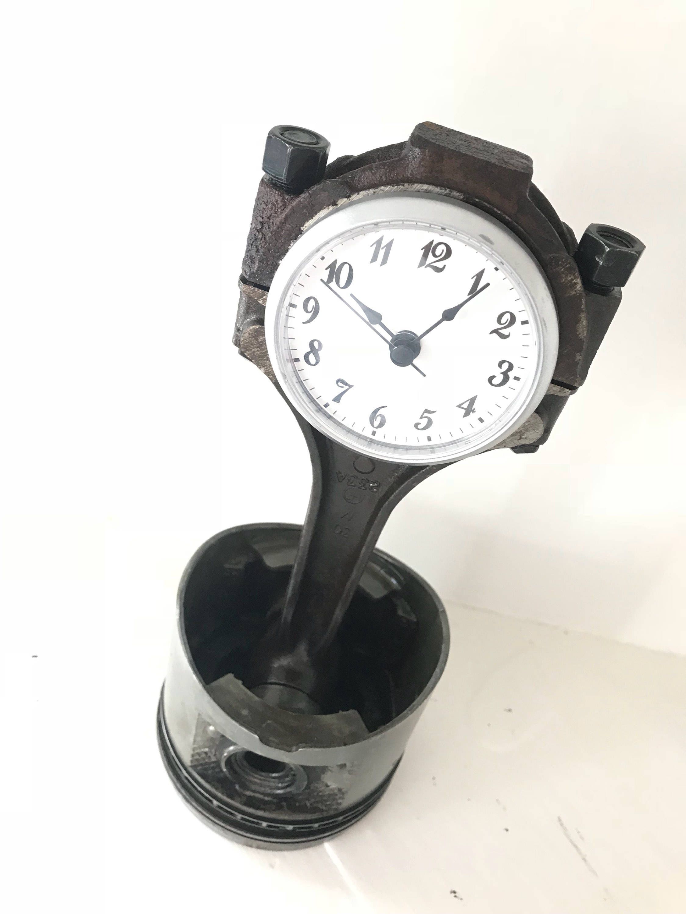 Clock made out of a car engine's piston in a patina finish with a silver clock ring.