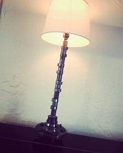 Lamp made out of a car's camshaft with its shade and turned on.