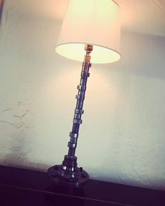 Silver lamp made out of a car's camshaft with its shade and turned on.