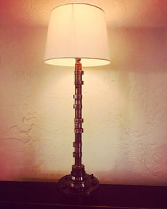 Lamp made out of a car's camshaft with its shade and turned on.