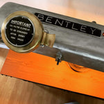 Load image into Gallery viewer, Close-up view of a desk lamp made from a car&#39;s valve cover, the Bentley logo displayed on top and including its oil filter holder, reading, &quot;Important - Oil filter element to be changed after every 5000 miles&quot;
