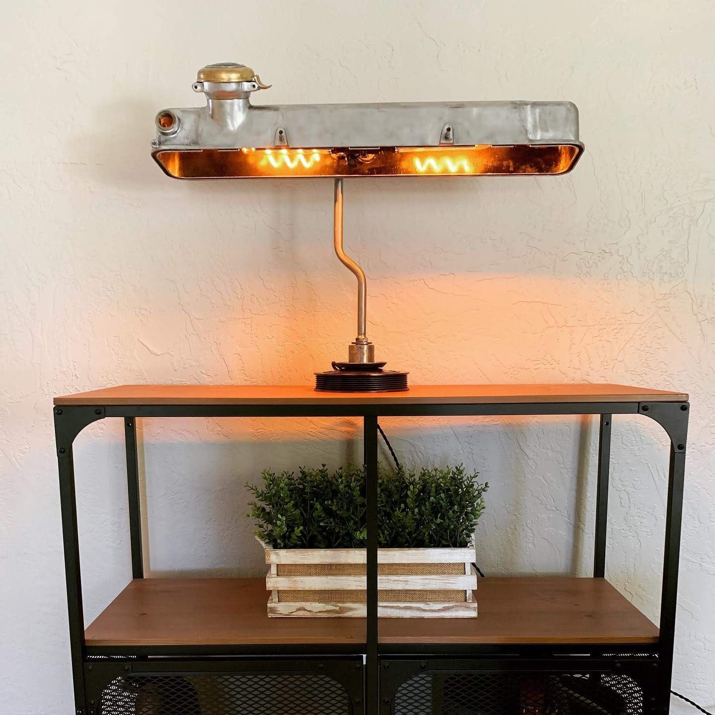 Desk lamp made out of a car's valve cover lit on top of an entryway table.