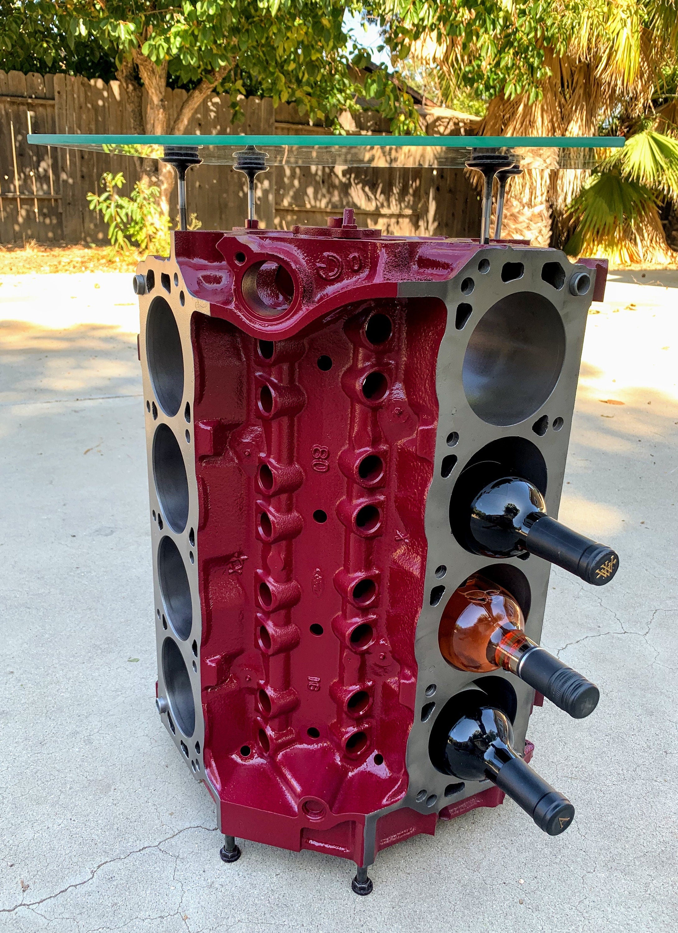 Engine block wine rack finished in red, with a square glass top and wine bottles stored in its side.
