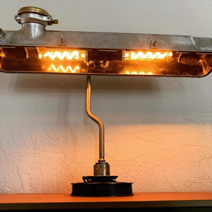 Desk lamp made from a car's valve cover turned on.