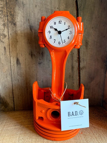Clock made out of a  car engine piston, painted bright orange.