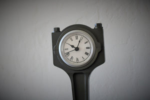 Close-up view of a piston clock made out of a Jaguar car's piston, finished in gunmetal gray with a silver clock ring.