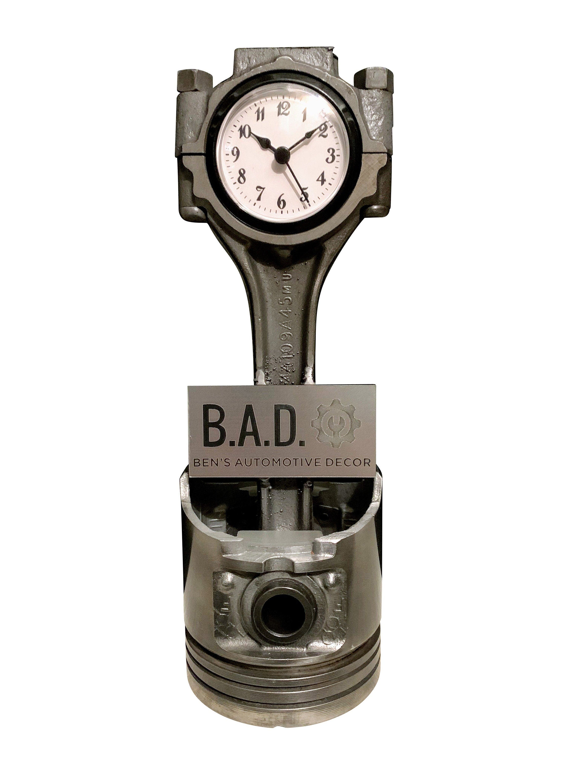 A piston clock finished in gunmetal gray with a black clock ring that includes a custom engraved plaque that reads, "B.A.D, Ben's Automotive Decor".