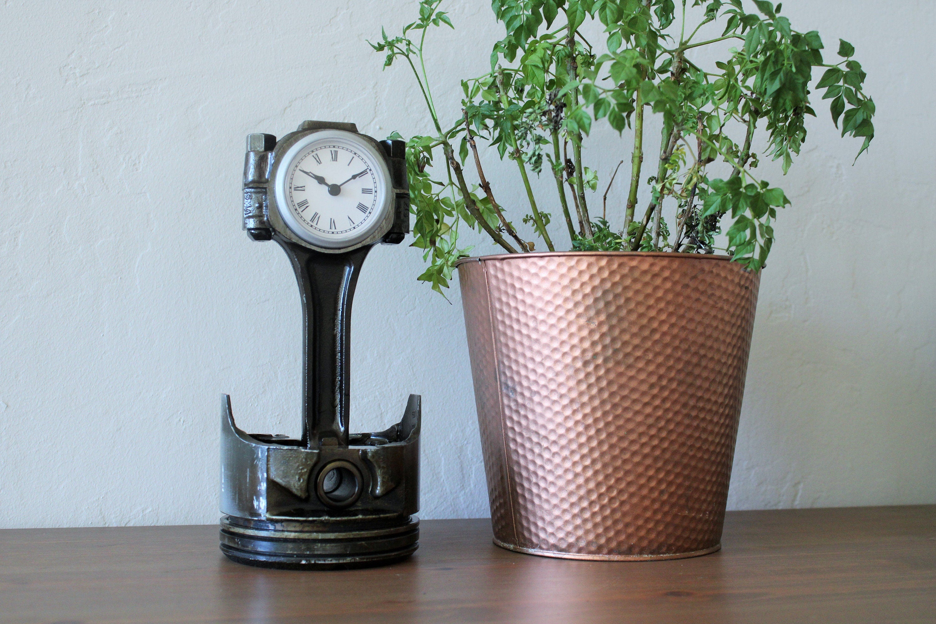 Clock made from a Chevrolet car's piston on a table next to a potted plant.