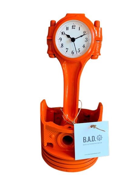 A piston clock finished in bright orange with a tag reading, "B.A.D., Ben's Automotive Decor".
