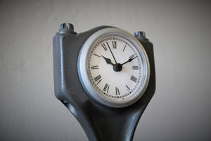 Close-up view of a clock made out of a car engine's piston, finished in gunmetal gray with a silver clock ring.