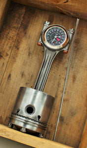 A piston clock made out of a Jaguar E-type XKE car piston, finished in gunmetal gray with a silver clock ring.