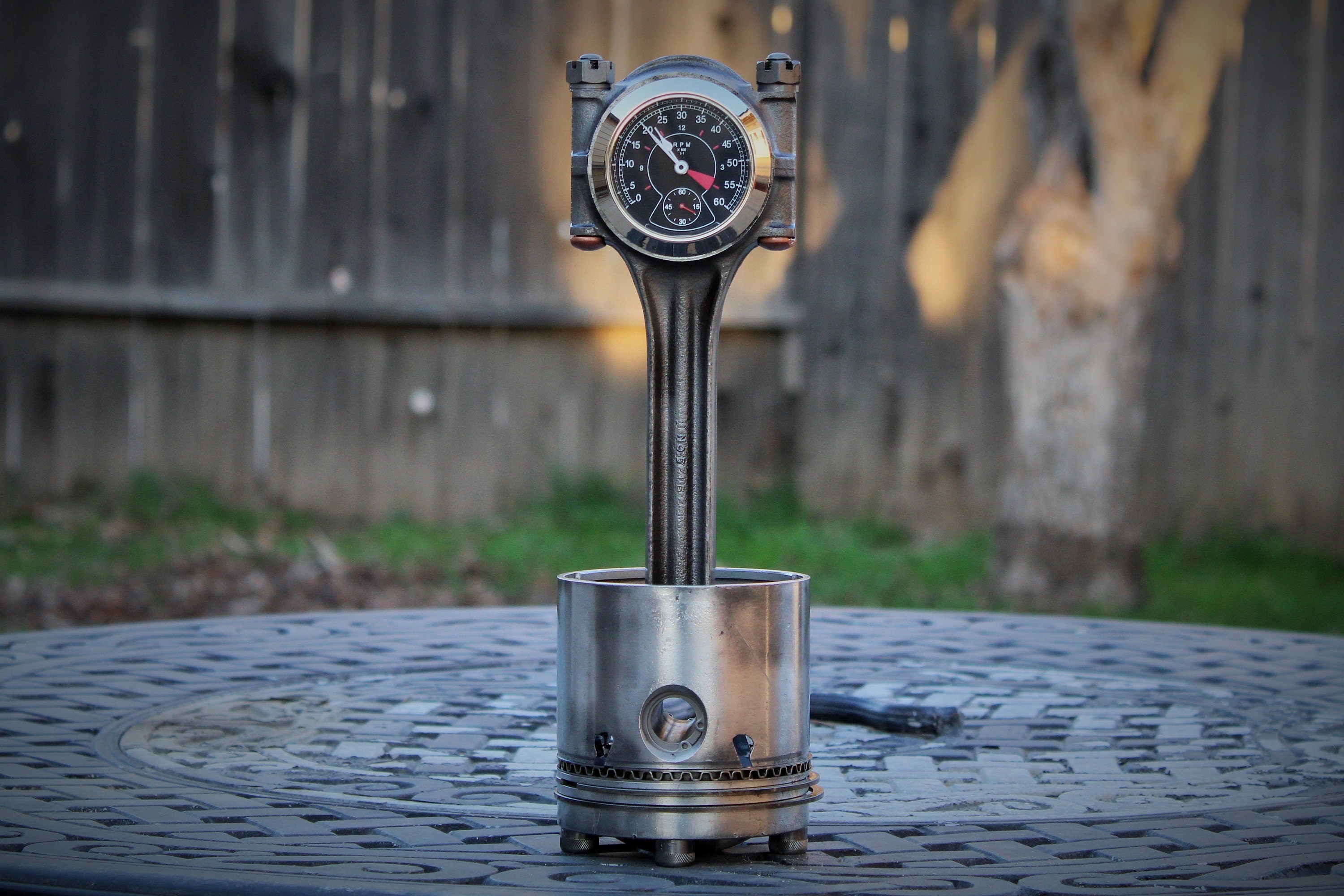 A piston clock made out of a Jaguar E-type XKE car piston, finished in gunmetal gray with a silver clock ring.