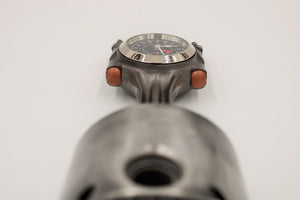 Close-up view of a piston clock made out of a Jaguar E-type XKE car piston, finished in gunmetal gray with a silver clock ring.
