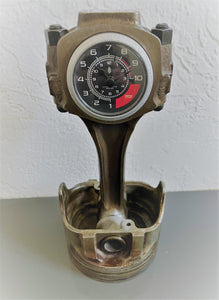 A car piston clock in a patina finish with a silver clock ring and black and red RPM clock face.