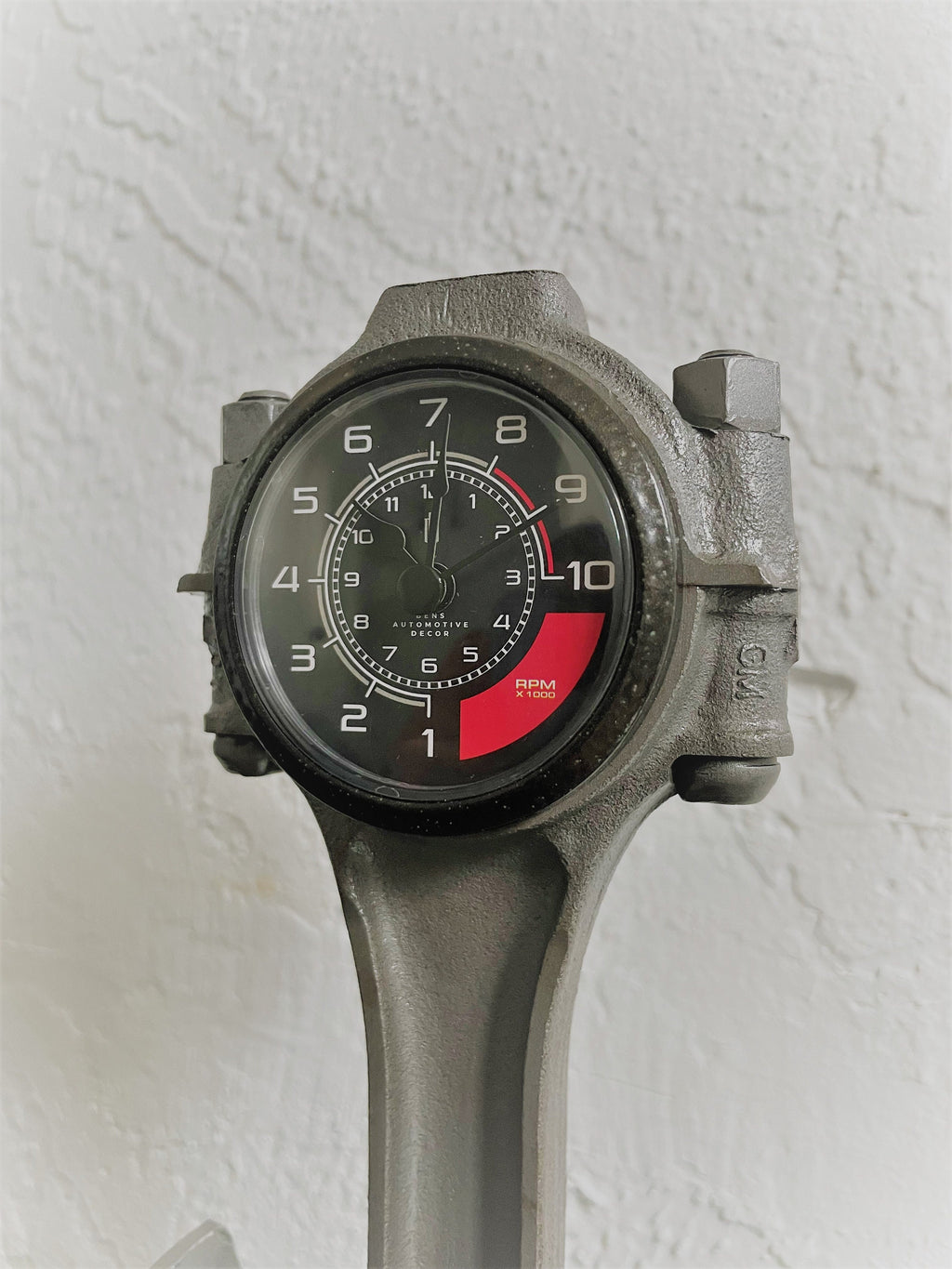 Close-up view of a car piston clock finished in gunmetal gray with a black clock ring and black and red RPM clock face.