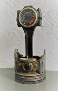 A car piston clock in a patina finish with a gold clock ring and black and red RPM clock face.