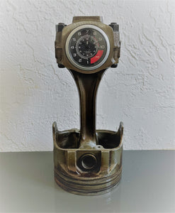 A car piston clock in a patina finish with a silver clock ring and a black and red RPM clock face.