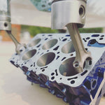 Load image into Gallery viewer, Close-up view of an engine block coffee table painted blue, its glass top being held up by car engine pistons.
