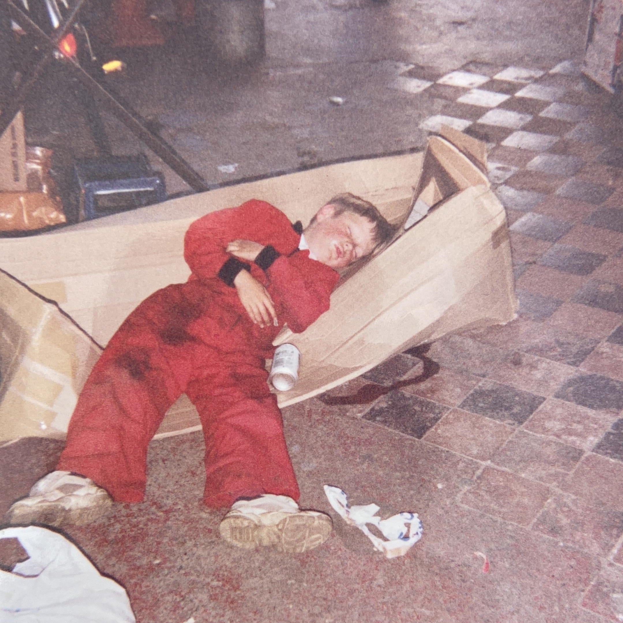 Child in a red snowsuit lying on a cardboard box on a sidewalk