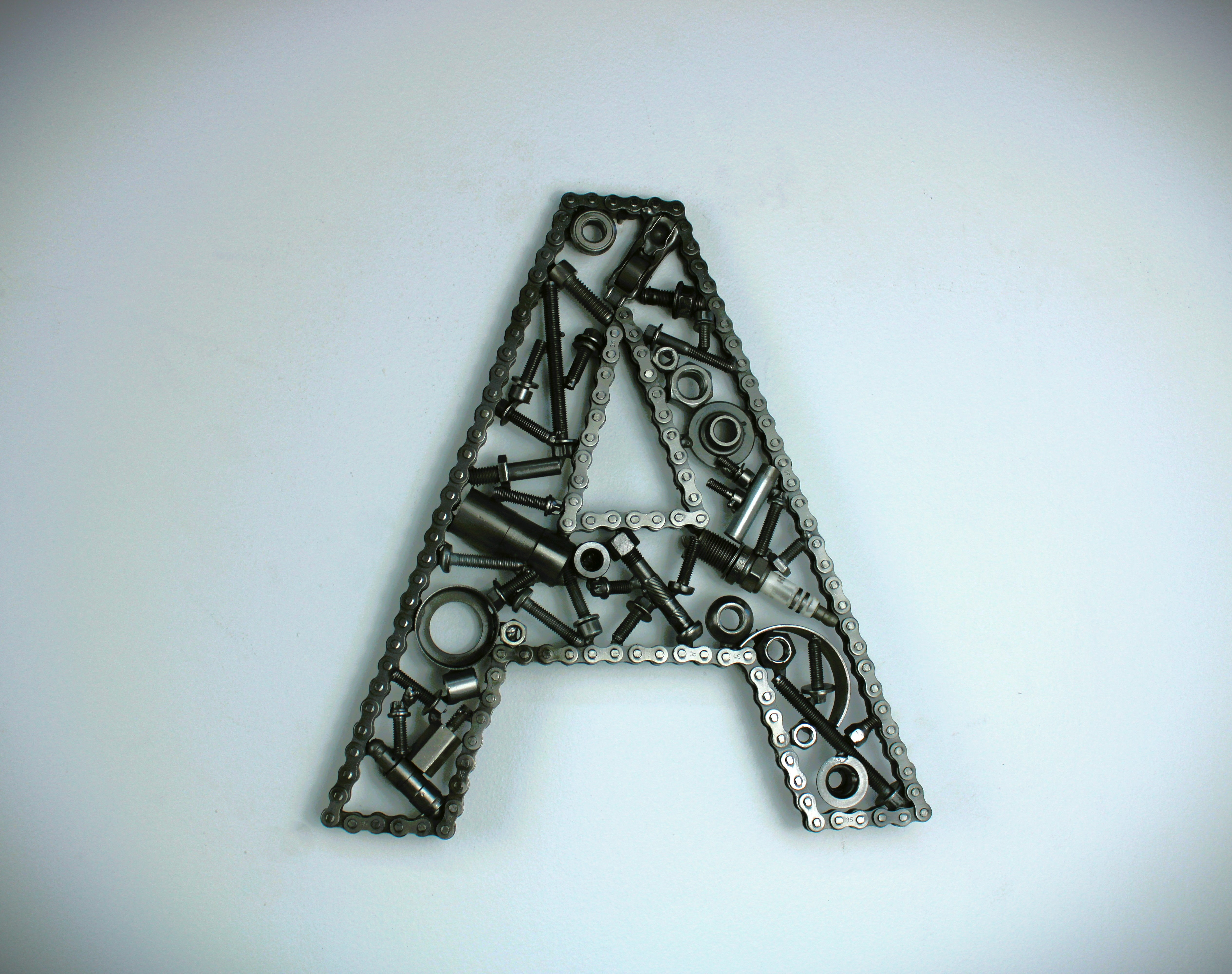A letter A made out of real car parts, outlined with a timing chain.