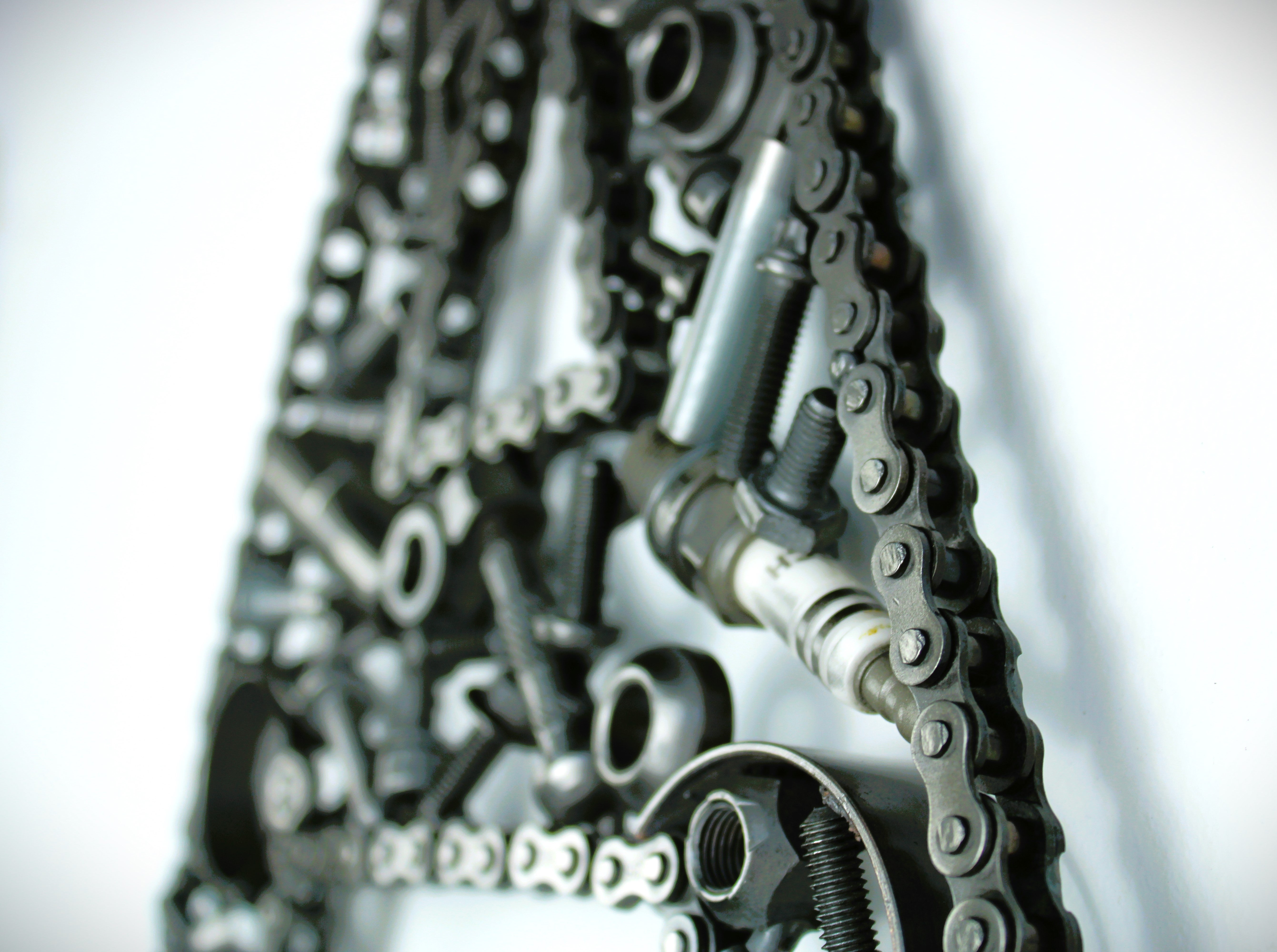 Close-up view of a letter A made out of real car parts, outlined with a timing chain.
