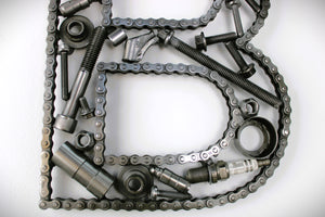 Close-up view of a letter B made out of real car parts, outlined with a timing chain.