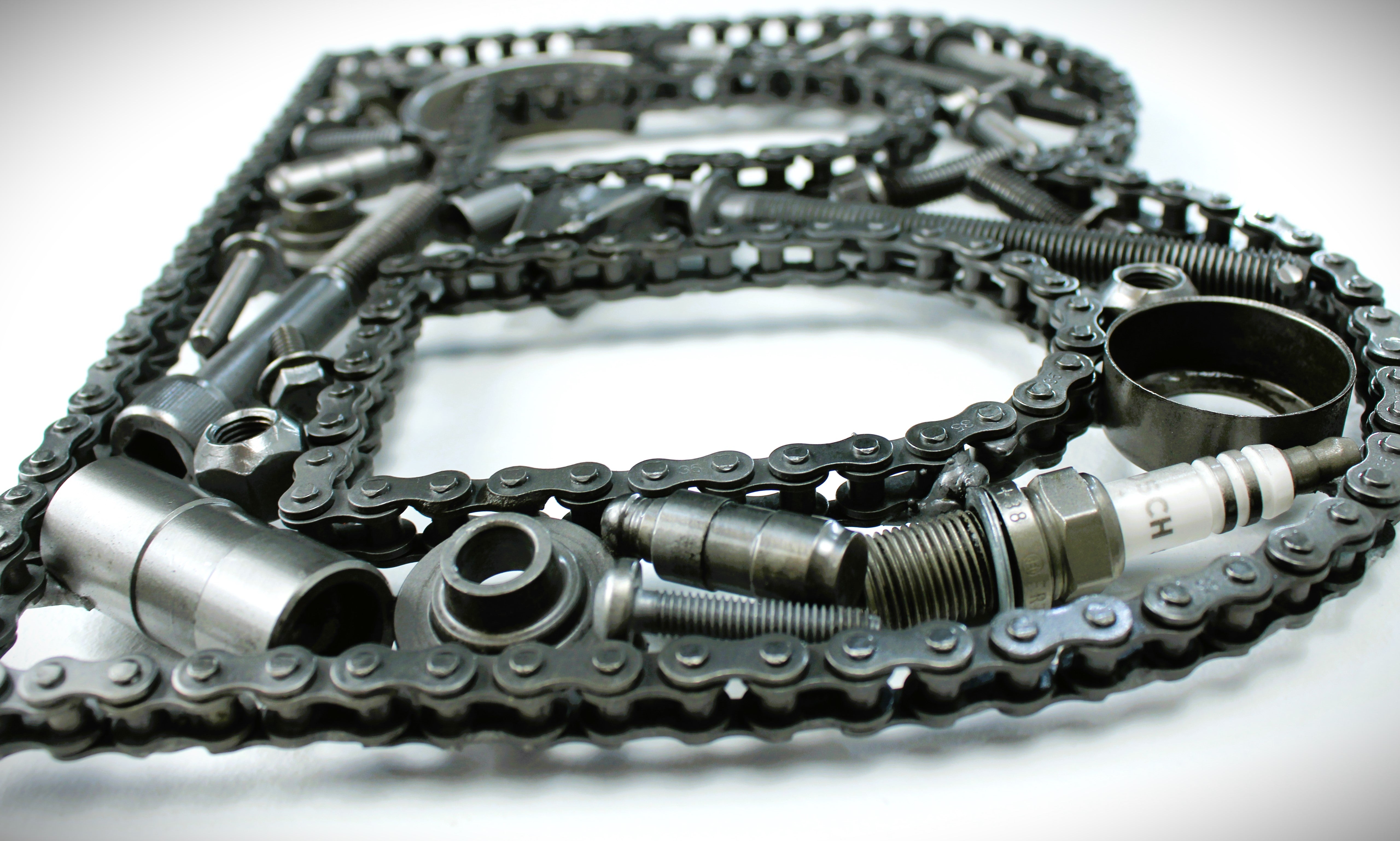Close-up view of a letter B made out of real car parts, outlined with a timing chain.