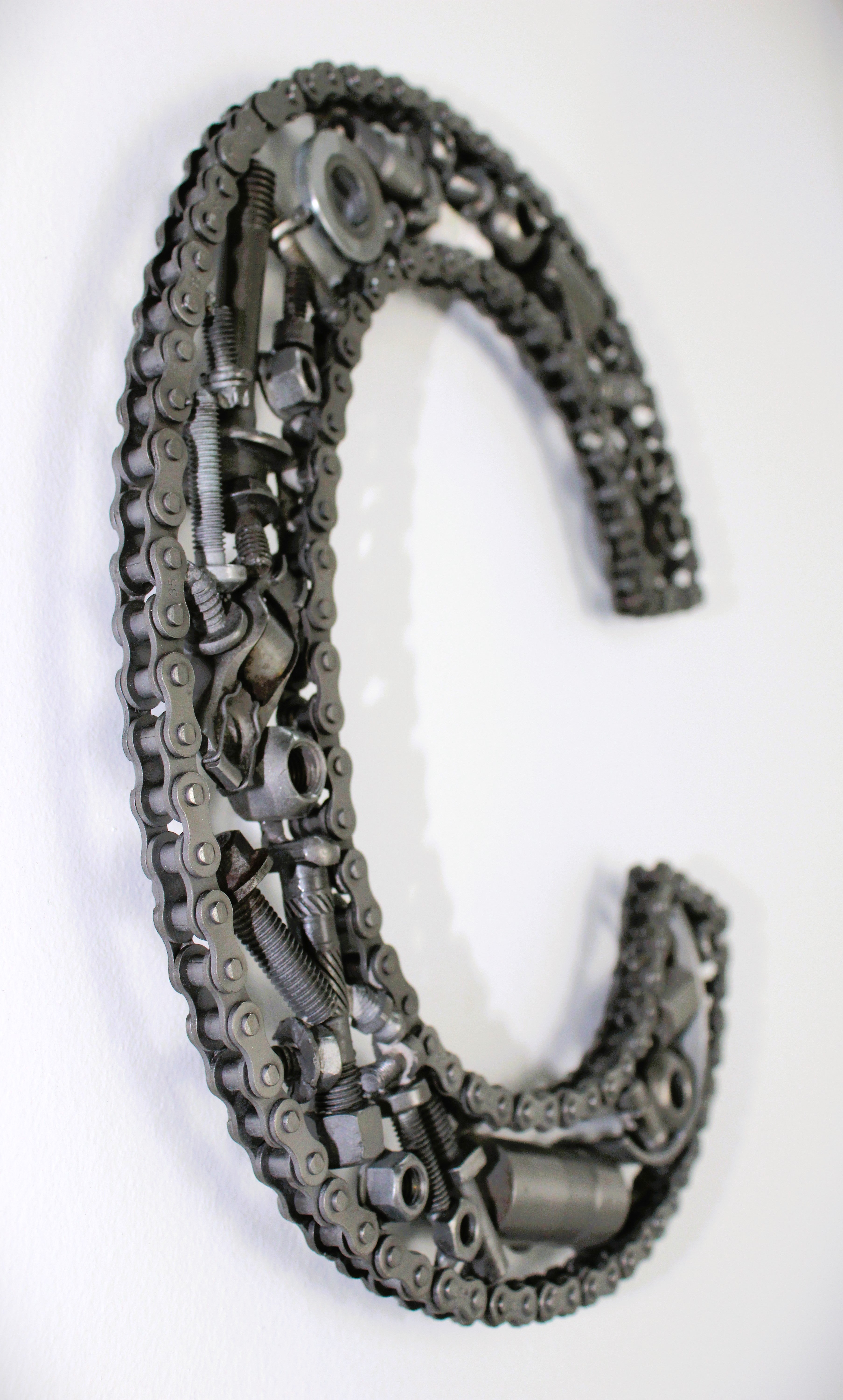 A letter C made out of real car parts, outlined with a timing chain.