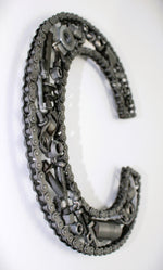 Load image into Gallery viewer, A letter C made out of real car parts, outlined with a timing chain.
