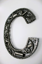 Load image into Gallery viewer, A letter C made out of real car parts, outlined with a timing chain.
