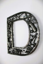 Load image into Gallery viewer, A letter D made out of real car parts, outlined with a timing chain.
