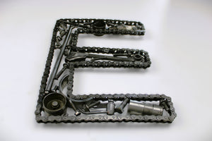 A letter E made out of real car parts, outlined with a timing chain.