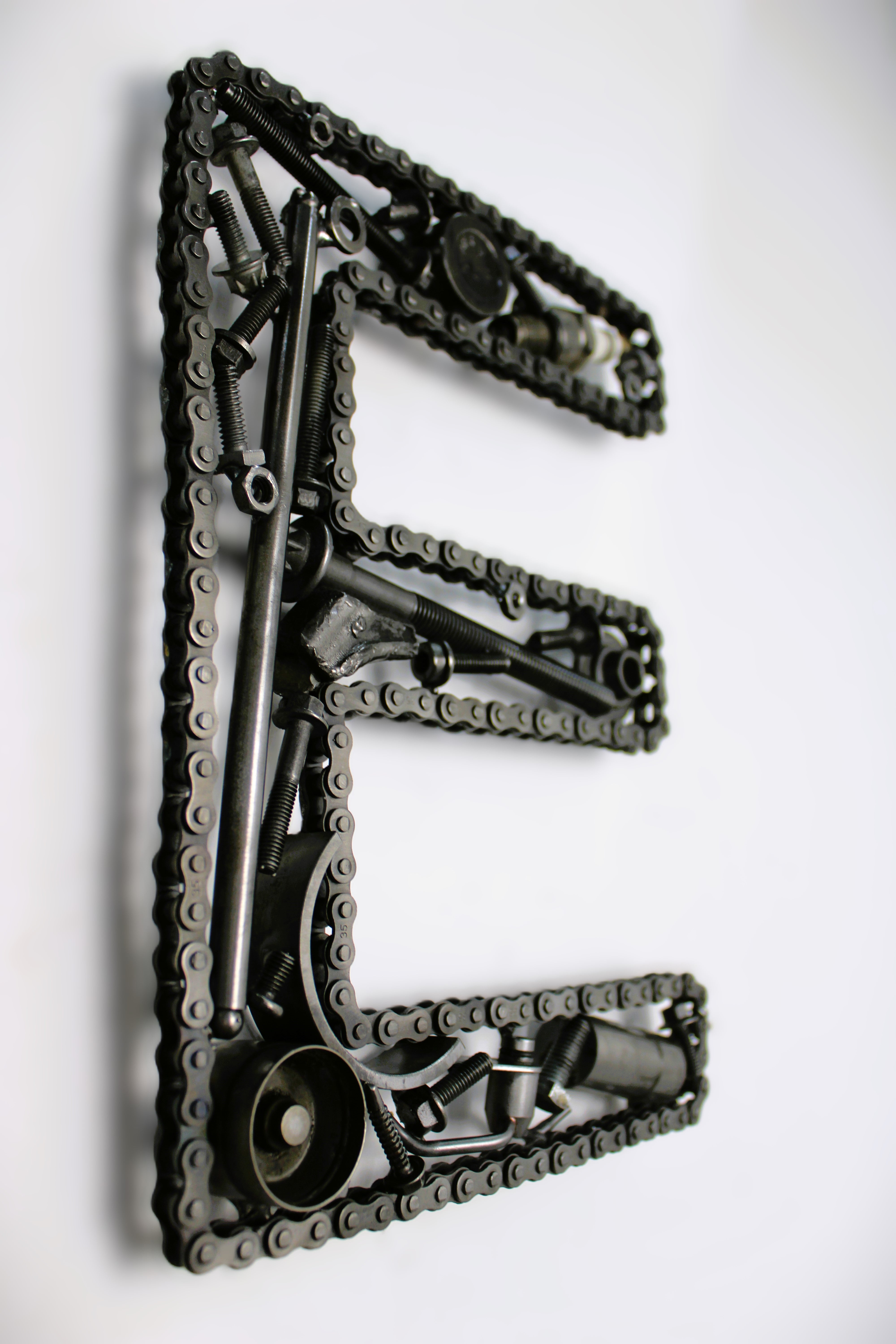 A letter E made out of real car parts, outlined with a timing chain.