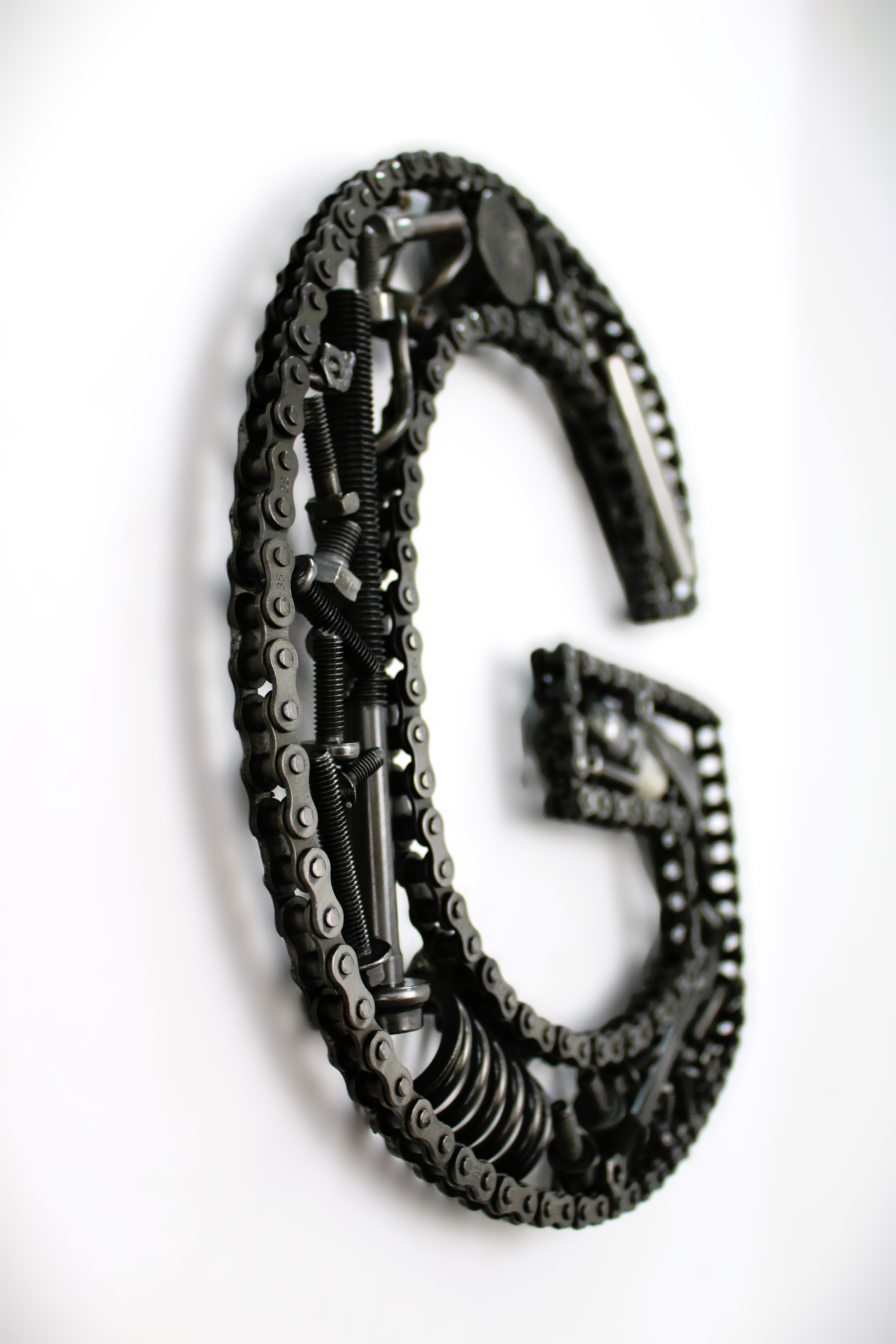 A letter G made out of real car parts, outlined with a timing chain.